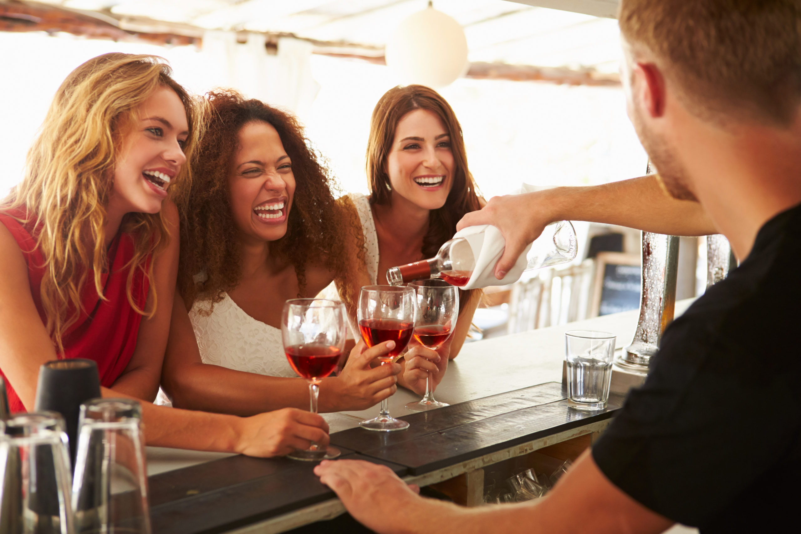 Three happy women drinking wine at a bar